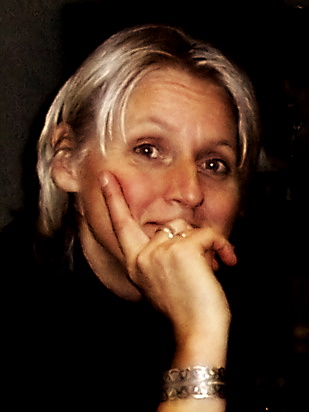 woman with short blonde hair, black sweater, rests chin in hand